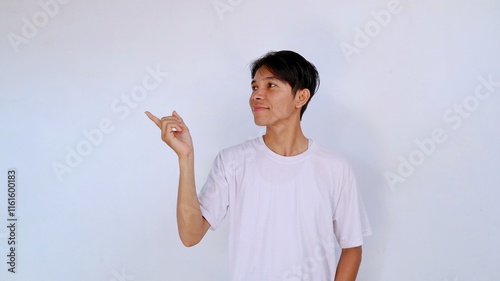 handsome asian young man wearing white shirt smiling while looking to the side and gesturing pointing to the side photo