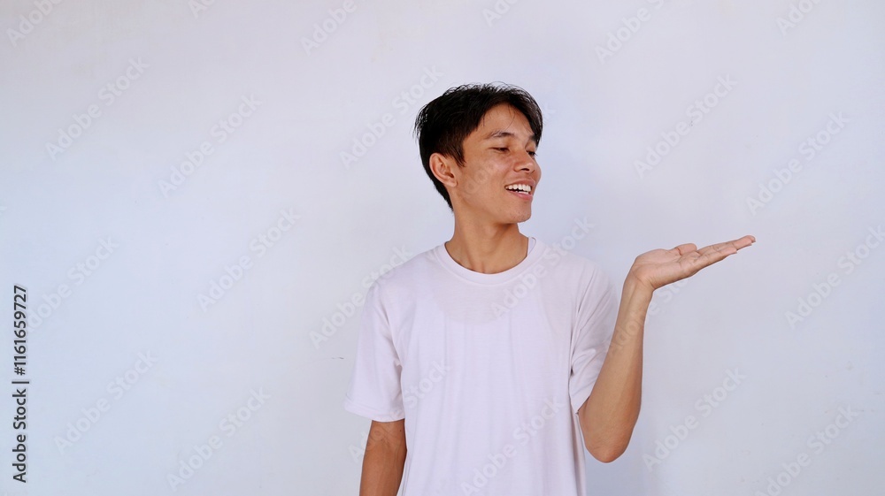 handsome asian young man smiling expression wearing white shirt gesture looking at open palm with isolated white background handsome asian young man smiling expression wearing white shirt gesture looking at open palm with isolated white background