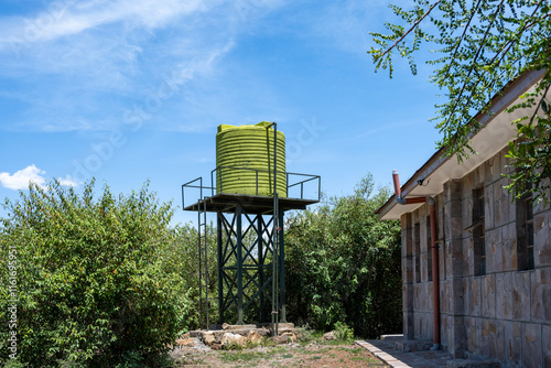 Modern green water raised water tank outside a stone building, in the Maasai Mara National Reserve, African wildlife adventure safari in Kenya
