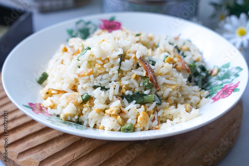 A plate of fried rice garnished with fresh green vegetables and anchovies, served on a floral-patterned plate.  Famously known in Malaysia as Nasi Goreng Kampung. photo