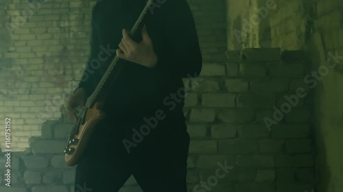 Close up of a musician energetically playing an electric bass guitar in a smoky, dimly lit room with a brick wall in the background, creating a dynamic and atmospheric musical scene