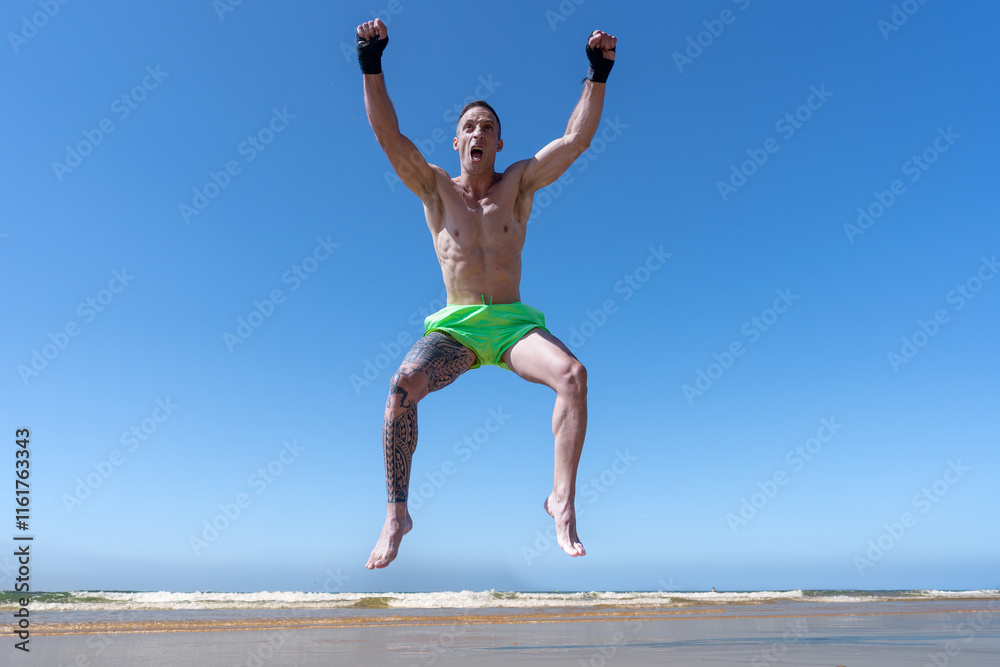 Obraz premium Hombre deportista en kick boxing saltando muy contento con los brazos en alto y los puños cerrados porque ha ganado y es el campeón.