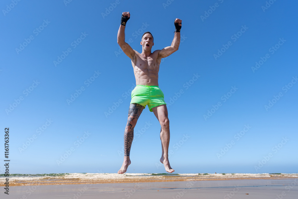 Obraz premium Hombre deportista en kick boxing saltando muy contento con los brazos en alto y los puños cerrados porque ha ganado y es el campeón.