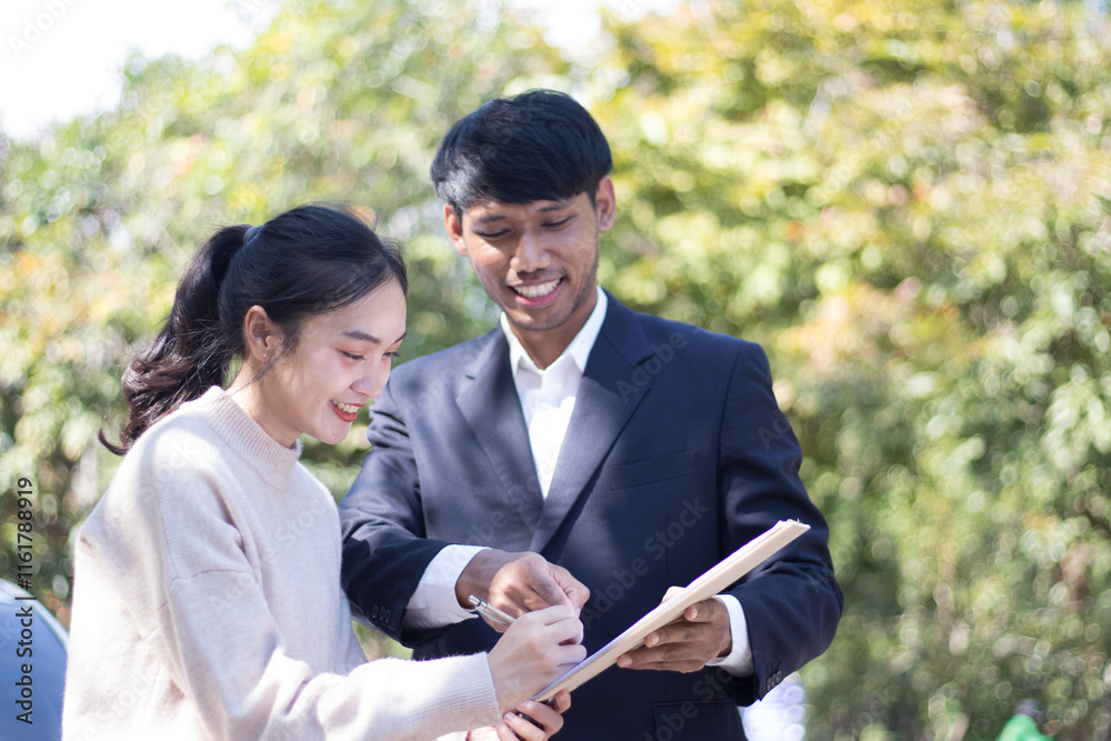 A young male car sales representative and a beautiful female customer are making a new car repair sign outdoors on a city road. A young male car sales representative and a beautiful female customer are making a new car repair sign outdoors on a city road.