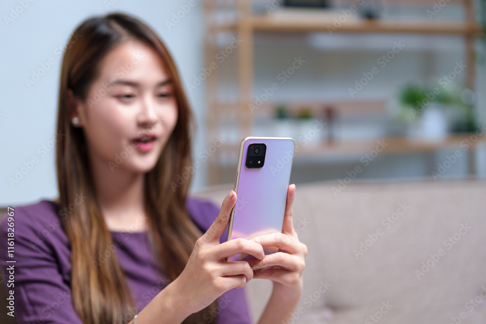 A young woman video calling on her smartphone while sitting on a sofa, engaging in a lively conversation A young woman video calling on her smartphone while sitting on a sofa, engaging in a lively conversation