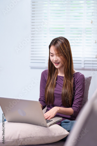 A young woman working on a laptop while sitting on a sofa, smiling and appearing focused, in a cozy home setting