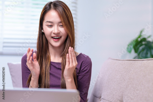 Free Download A woman enthusiastically engaging in an online meeting via laptop, clapping her hands while smiling, seated on a cozy sofa. - GFXLoad