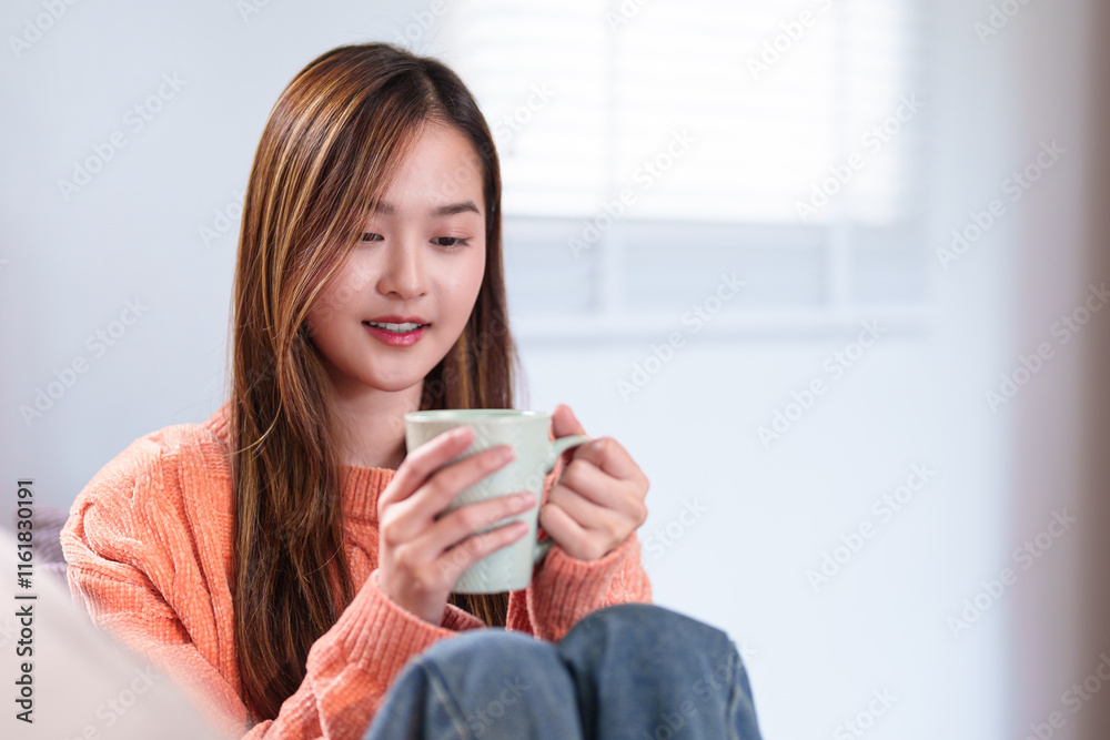 A young woman seated comfortably, holding a mug of coffee close, smiling softly, dressed in a cozy orange sweater, enjoying a peaceful moment. A young woman seated comfortably, holding a mug of coffee close, smiling softly, dressed in a cozy orange sweater, enjoying a peaceful moment.