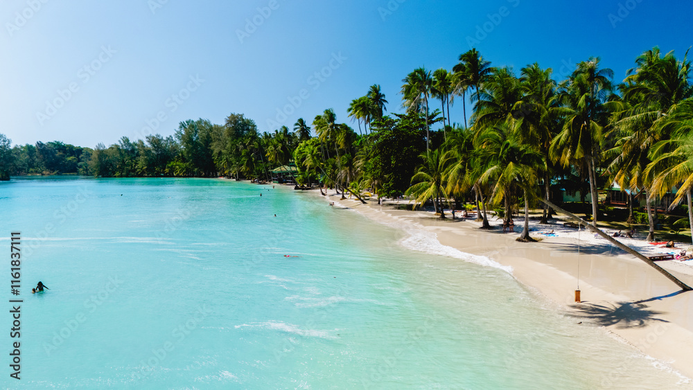 Clear turquoise waters gently lap against the soft white sand of a serene beach in Koh Kood. Lush palm trees sway as visitors relax and enjoy the tropical paradise during a sunny day. Clear turquoise waters gently lap against the soft white sand of a serene beach in Koh Kood. Lush palm trees sway as visitors relax and enjoy the tropical paradise during a sunny day.