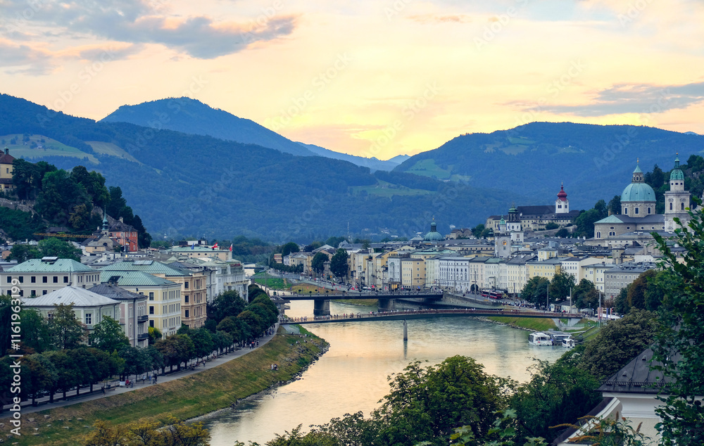 The city of Salzburg with historical buildings bisected by a winding Salzach River and mountain ranges in the background