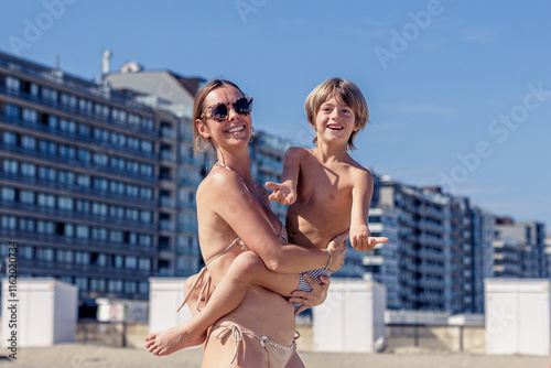 Obraz na plátne smiling mother proudly holds her playful son on a sunny beach