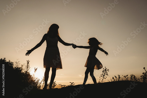 Mother and daughter silhouette dancing at beach on summer sunset