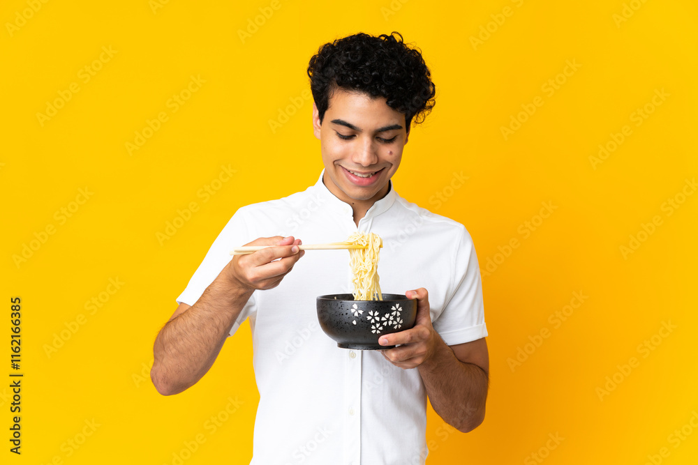 Young Venezuelan man isolated on yellow background holding a bowl of noodles with chopsticks Young Venezuelan man isolated on yellow background holding a bowl of noodles with chopsticks
