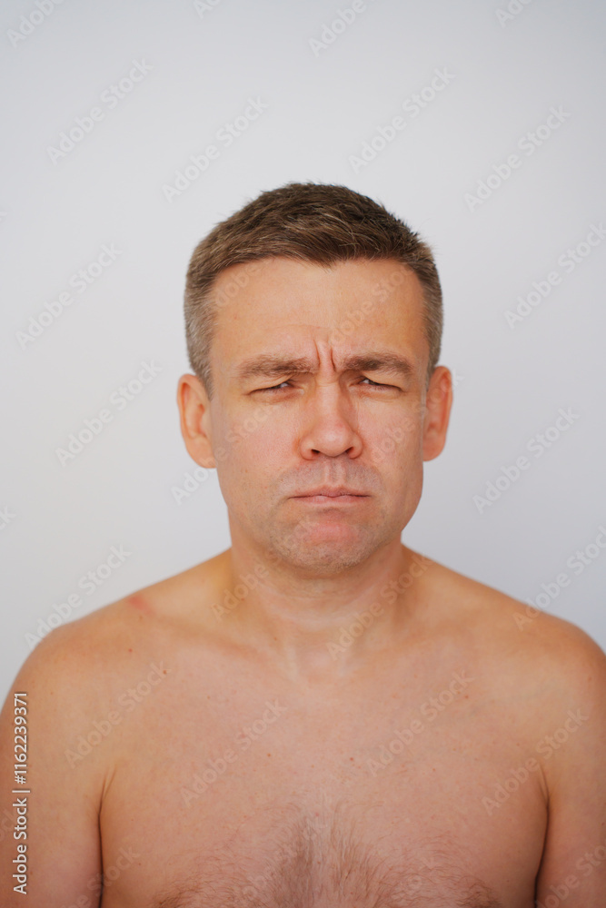Portrait of a grimacing middle-aged man with a naked torso on a white background. photo posing. men's physical and mental health Portrait of a grimacing middle-aged man with a naked torso on a white background. photo posing. men's physical and mental health