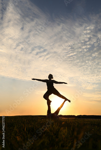 Wallpaper Mural Young adult sports couple doing acro yoga exercises. Silhouette couple practicing yoga at sunset. woman, man do acroyoga. sporty healthy pair doing acrobatic yoga at sunrise. female stand on foot Torontodigital.ca