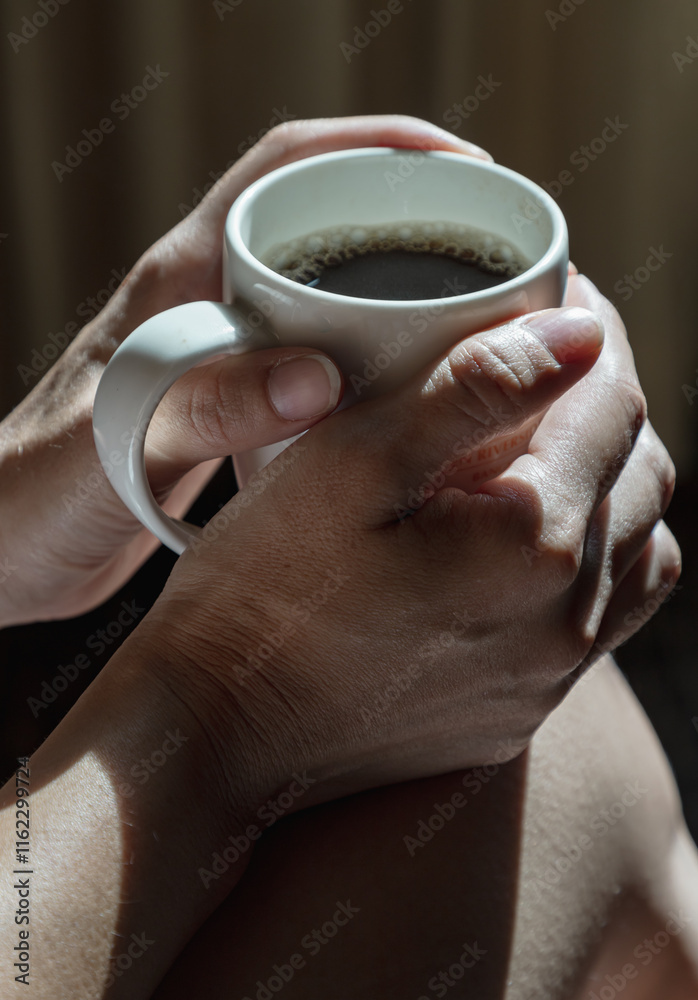 Close-up of Comforting cozy female hands holding a coffee mug with the morning sunlight that shines through. Dark tone, use it as your Wallpaper, Poster and Copy space, Selective focus.