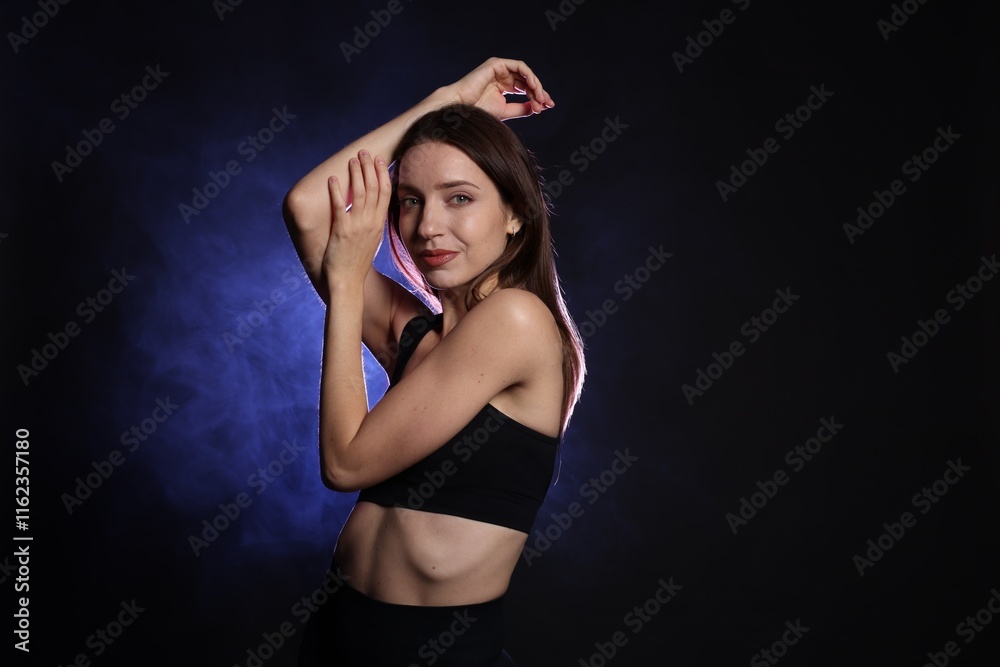 Beautiful woman in stylish sportswear on dark background with color light and smoke Beautiful woman in stylish sportswear on dark background with color light and smoke