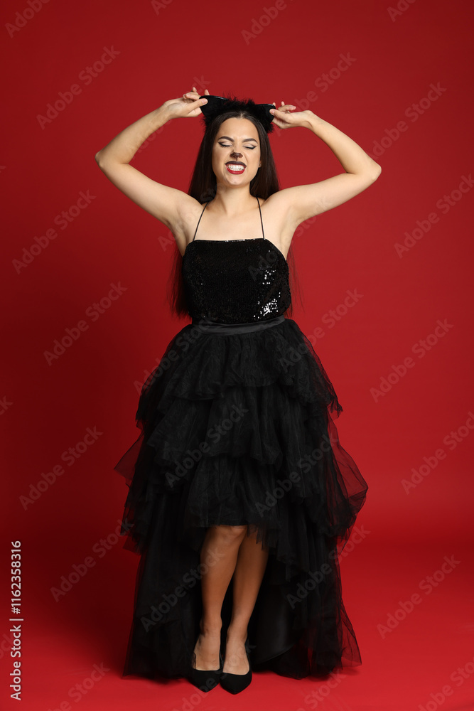Woman with cat makeup and ears in beautiful dress on red background Woman with cat makeup and ears in beautiful dress on red background