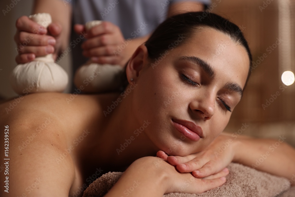 Woman receiving back massage with herbal bags in spa salon Woman receiving back massage with herbal bags in spa salon
