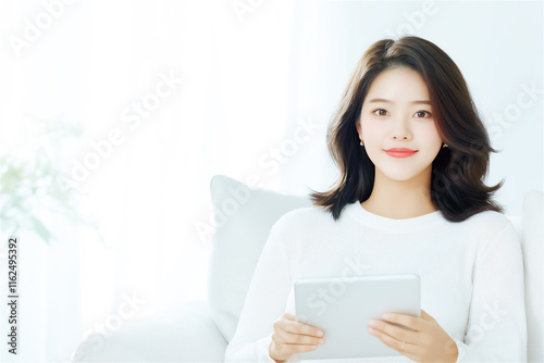 Young woman in a white shirt sitting comfortably, holding a tablet, with a serene background. A concept of modern technology and relaxation.