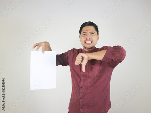 Handsome Asian man in red shirt holding blank white paper with a gesture of disapproval, dislike and disappointed expression while thumbs down photo