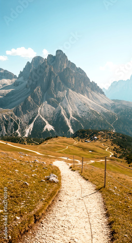 Scenic mountain pathway through dolomites with clear blue sky and rolling hills