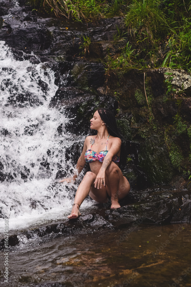 Fototapeta premium Mulher sentada sobre a rocha, numa cascata