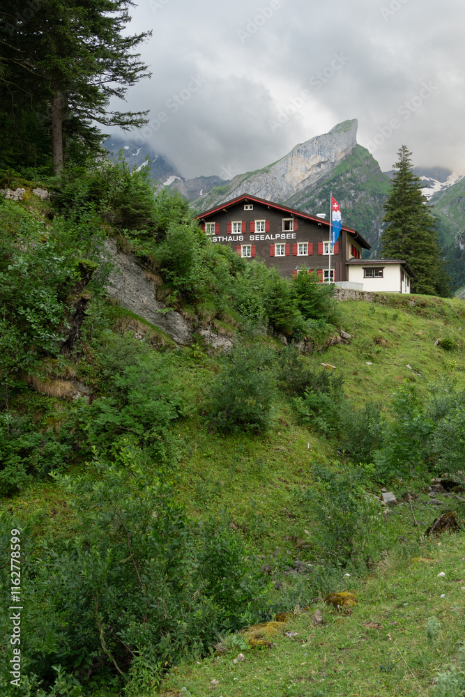 Evening view of the Swiss mountain hut at the Seealpsee lake in the Appenzeller Alps. Mountain refuge surrounded by steep Alpine mountains and pine trees in Switzerland. Beautiful hiking spot. Evening view of the Swiss mountain hut at the Seealpsee lake in the Appenzeller Alps. Mountain refuge surrounded by steep Alpine mountains and pine trees in Switzerland. Beautiful hiking spot.