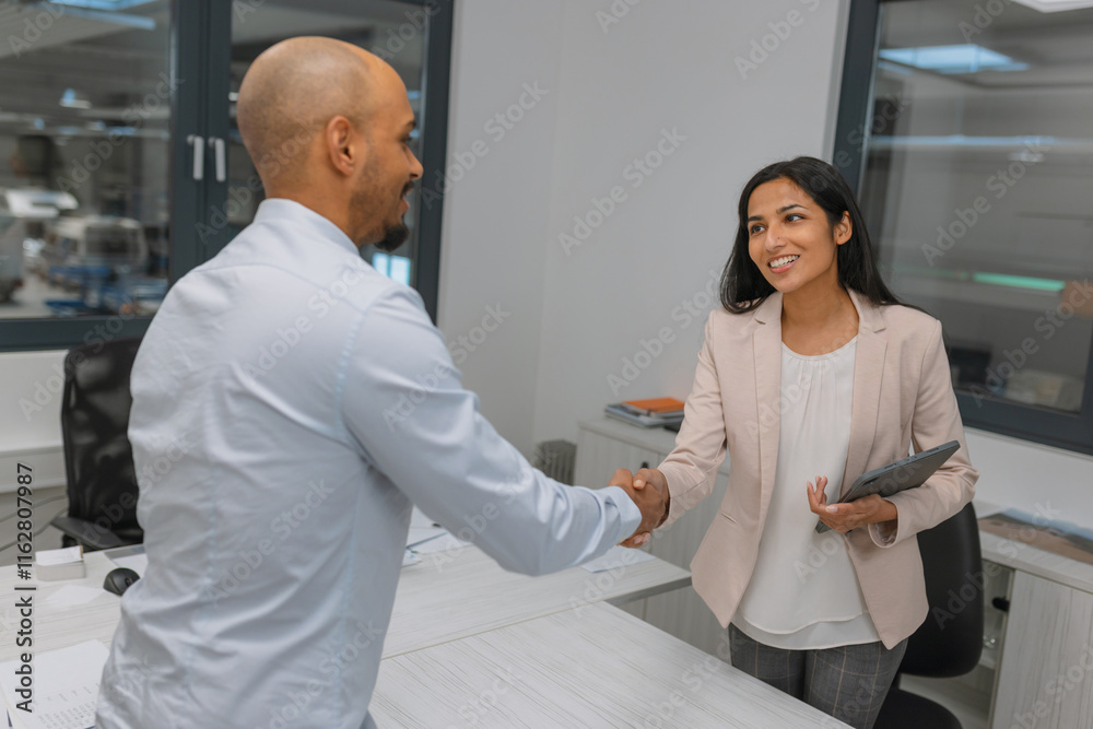 Obraz premium Indian woman, a prosperous company manager shaking hands with a job applicant, a young African American man, after a successful employment interview.