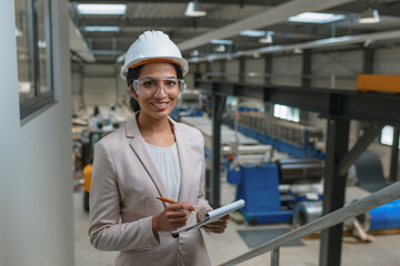Young Indian woman, a successful metalworking factory manager writing notes after production inspection, smiling portrait shot.