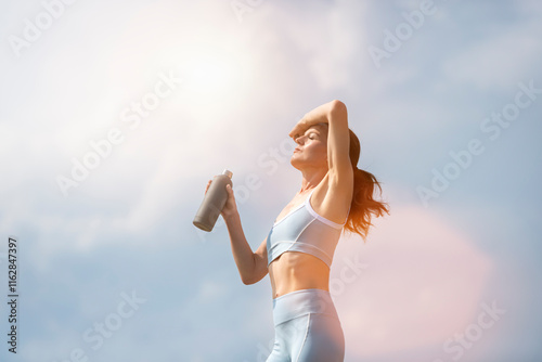 fit sporty woman standing in the sun holding a bottle of water, heatwave concept. photo