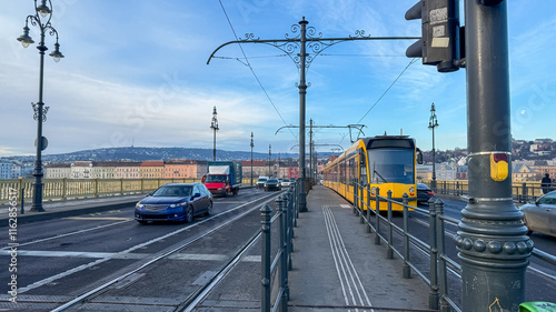 A yellow tram traverses a historic European bridge in Budapest, highlighting urban transportation concepts during winter travel season