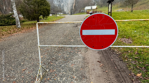 A weathered no-entry sign blocks a rural path in a serene autumn park, symbolizing restricted access and solitude