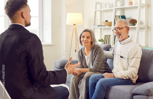 Gray-haired happy smiling senior couple sitting on sofa in the living room at home and having consultation with a male financial advisor about health insurance. Investment in retirement concept photo