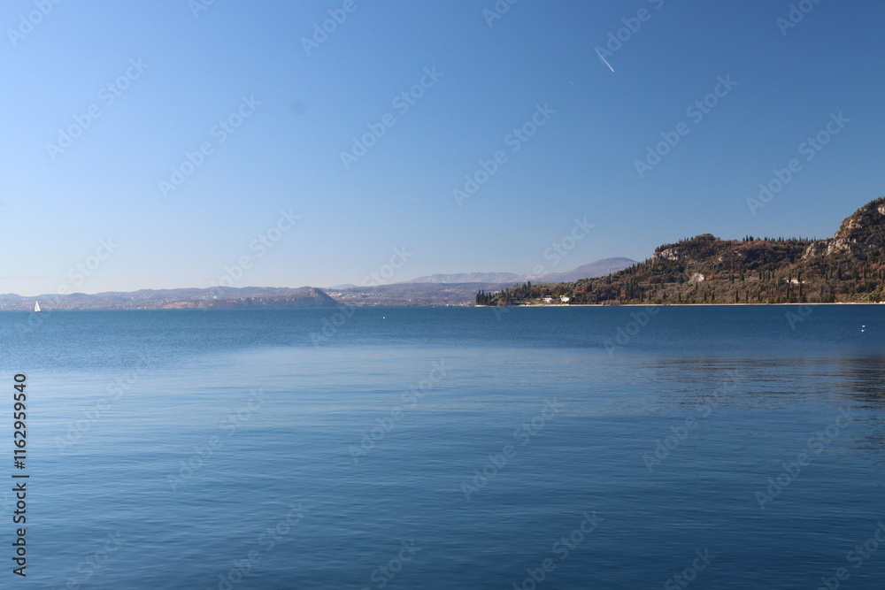 Sailboat navigating calm waters of lake garda near the rocca di manerba Sailboat navigating calm waters of lake garda near the rocca di manerba