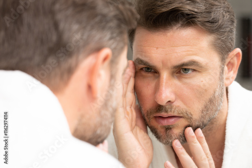 a well-groomed adult man looks in the mirror for well-groomed, wrinkle-free skin. Handsome man checking wrinkles in mirror at home. Man in front of mirrror looking at his wrinkles
