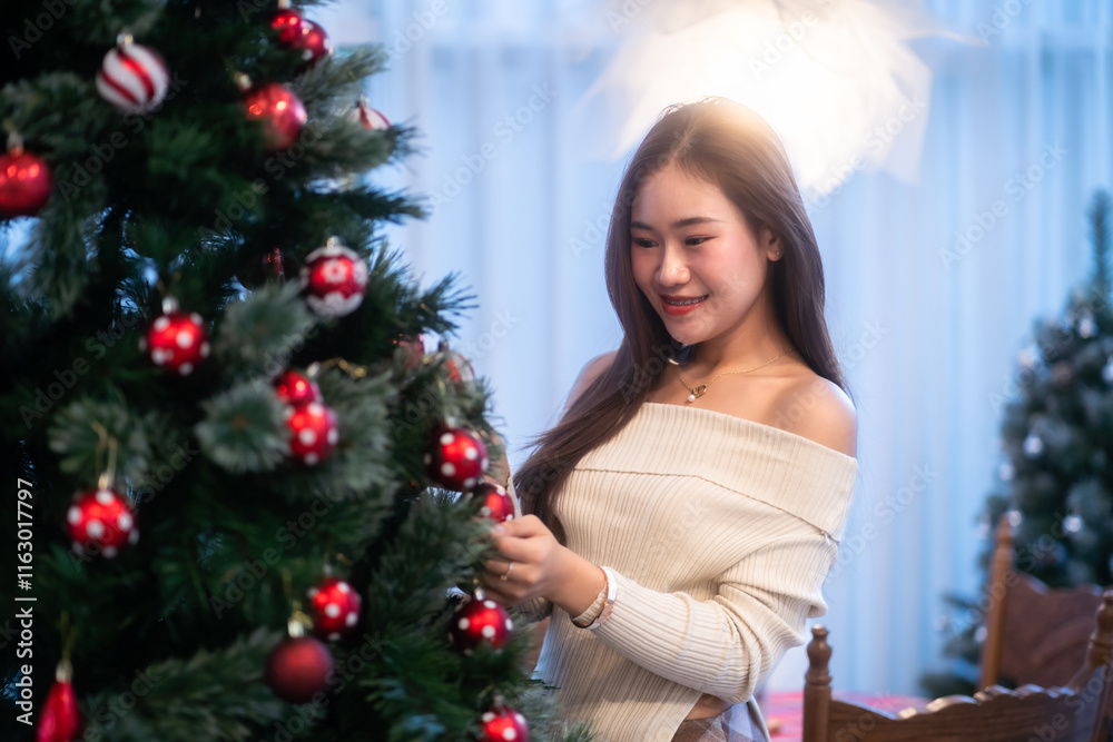 Portrait of beautiful happy Smiling asian woman relaxing sitting decorating to a Christmas tree at home in the living room indoors Decoration During Christmas x-mas and New Year holidays.