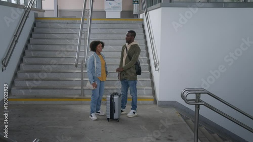 African American tourists with a suitcase, standing at a train station talking while waiting for departure time, handheld shot.