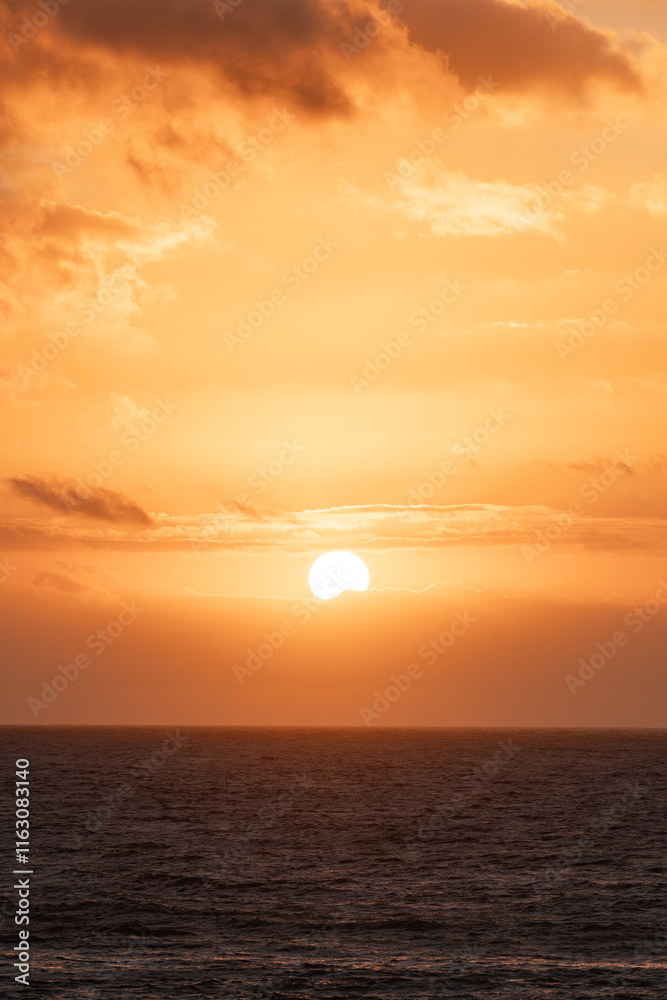 Vertical sunset over the ocean creates a vibrant orange sky and calm waters Vertical sunset over the ocean creates a vibrant orange sky and calm waters