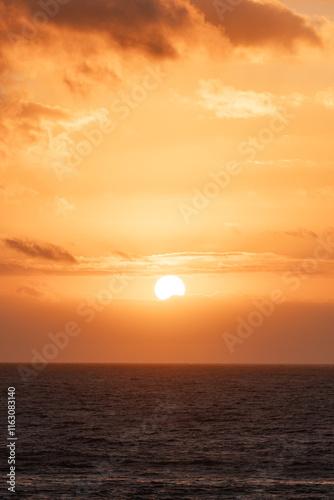 Vertical sunset over the ocean creates a vibrant orange sky and calm waters