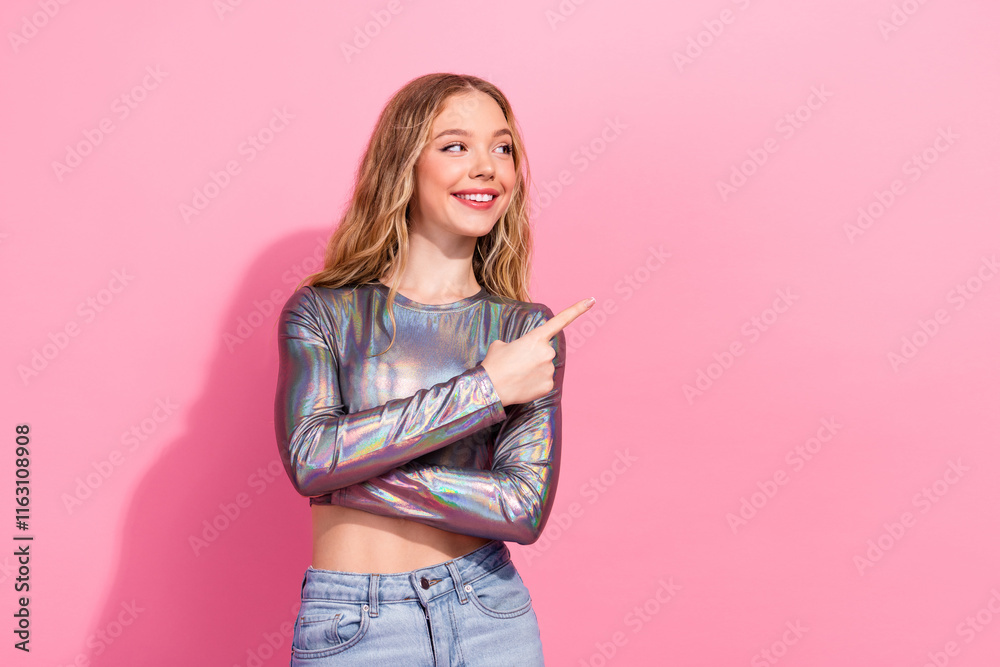 Smiling blonde woman in shiny top pointing sideways against vibrant pink backdrop. Smiling blonde woman in shiny top pointing sideways against vibrant pink backdrop.