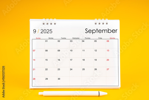 September 2025, Monthly desk calendar for 2025 year and pen on yellow background. photo