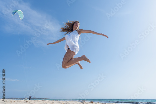 Mujer joven saltando de emoción porque esta muy a gusto, con un sensacional día de vacaciones en verano soleado con cielo azul.