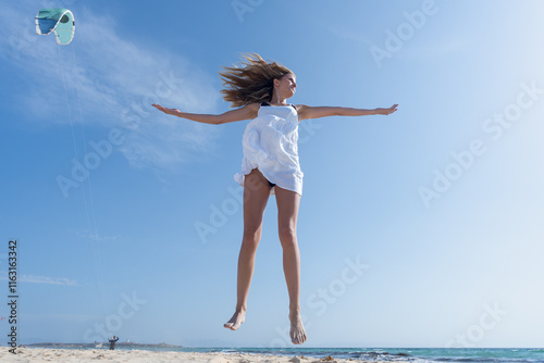 Mujer joven saltando de emoción porque esta muy a gusto, con un sensacional día de vacaciones en verano soleado con cielo azul. photo