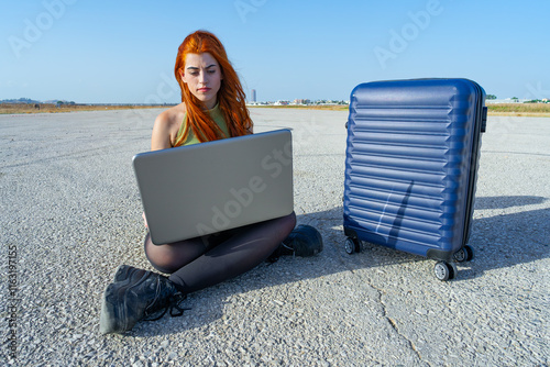 Chica viajera nómada digital trabajando en la pista de aterrizaje de un aeropuerto conectada a internet, un día soleado con cielo azul.