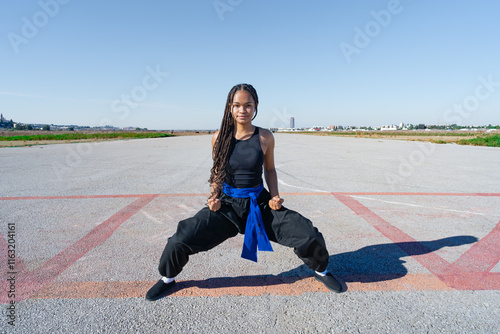 Chica joven luchadora de artes marciales en el paisaje infinito y minimalista de una pista de aterrizaje un día soleado de verano con cielo azul.