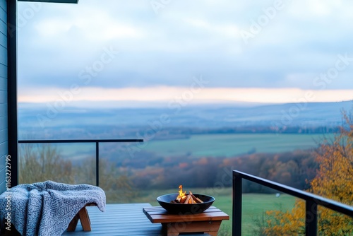 A cozy balcony with a high view of rolling hills, a small fire bowl, and a blanketdraped bench photo