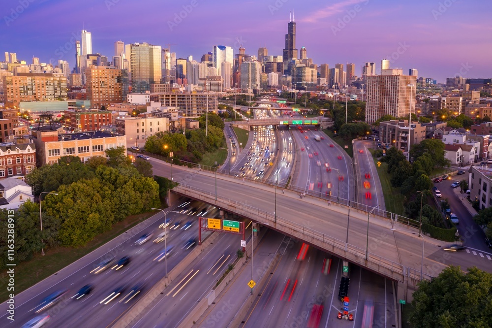 Obraz premium Chicago highway traffic at dusk. Cars blur across the interstate, under a highway overpass, as the sun sets over the city skyline. Interstate 90, Chicago, Illinois, United States