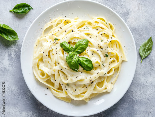 Classic Fettuccine Alfredo pasta garnished with fresh basil and black pepper in a white plate.