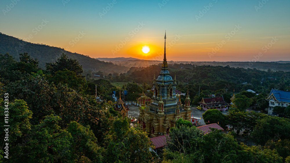 Fototapeta premium Aerial view of Mae Klang Waterfall Temple in Chiang Mai with the sunrise casting warm hues in calm sky. The tranquil setting highlights the serene beauty of the temple and the natural landscape.